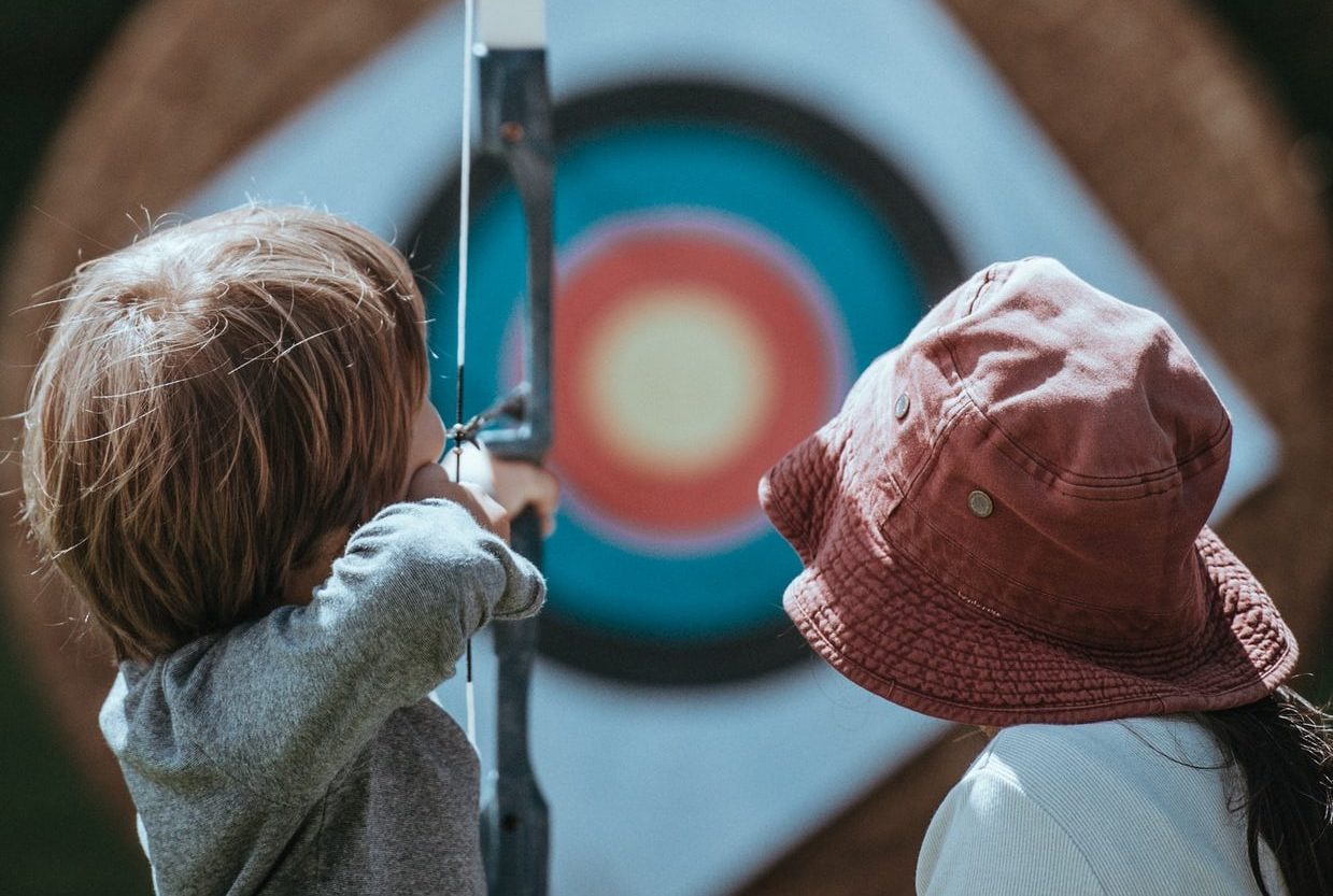 boy aiming bow and arrow at target